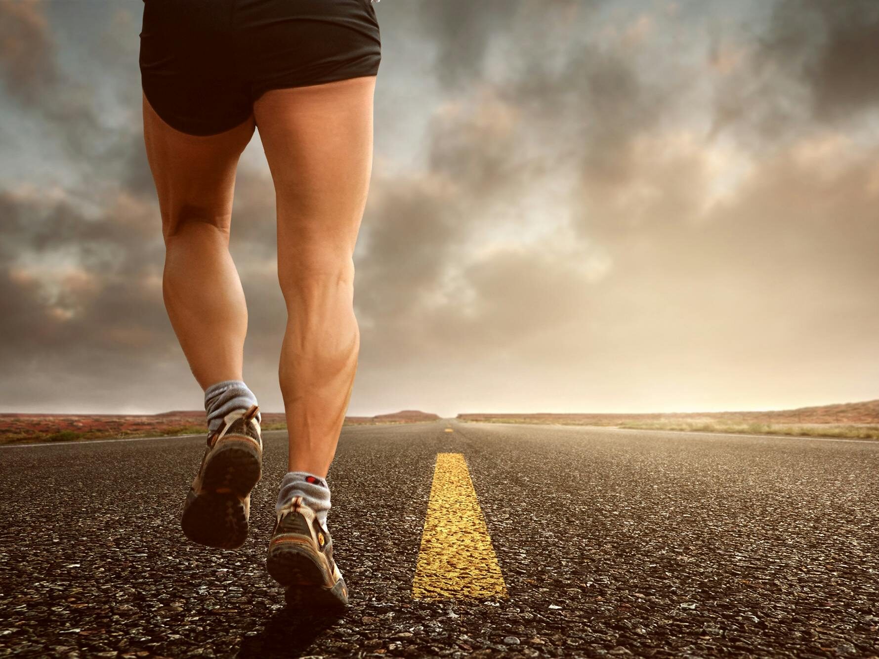 Runner's legs on a road during a sunset, symbolizing endurance and outdoor fitness training.